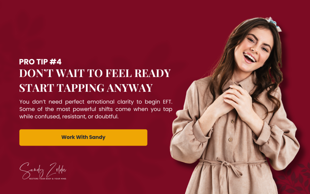  A woman in a beige dress with a bow in her hair stands against a red background. Text reads: "Don’t Wait to Feel Ready Start Tapping Anyway," encouraging EFT even when confused or resistant, by Sandy Zeldes, for powerful emotional shifts.