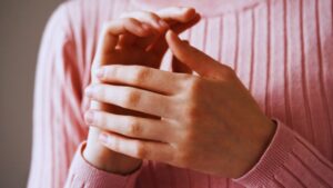 Person performing EFT tapping on hand/karate chop point in pink sweater, demonstrating practical emotional freedom technique methods for managing sugar cravings and achieving lasting behavioral change.