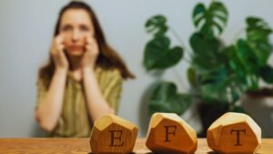 Woman practicing EFT tapping with wooden blocks spelling EFT, demonstrating tapping script for weight loss that calms cravings and addresses emotional eating at the root