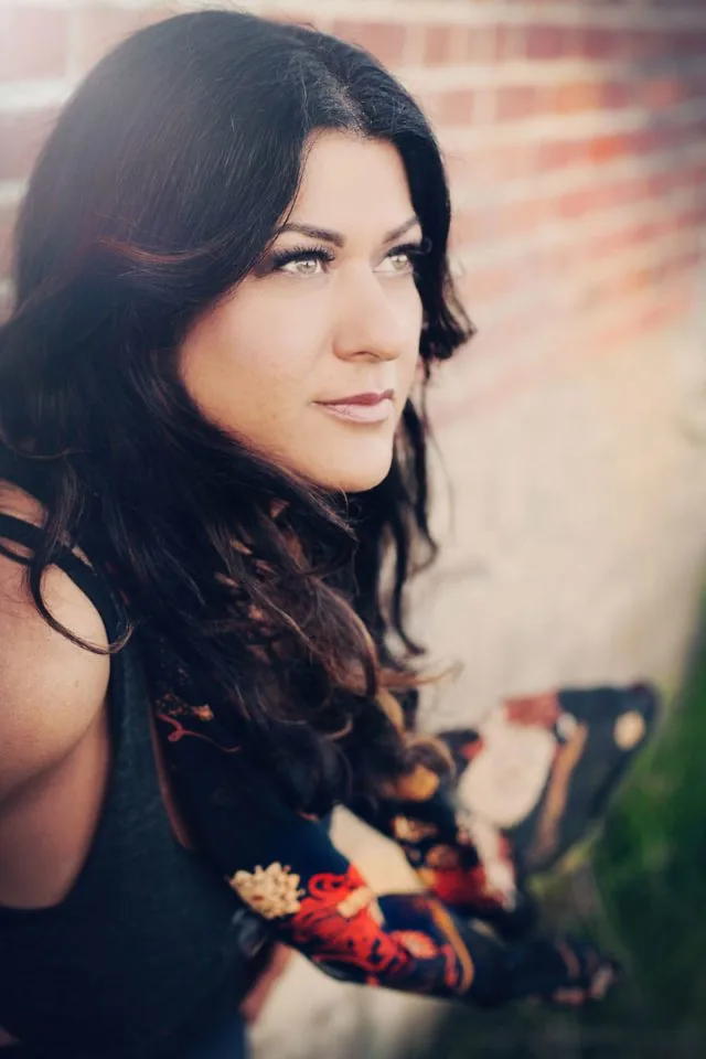 A profile portrait of a woman with long, dark, wavy hair looking off into the distance.